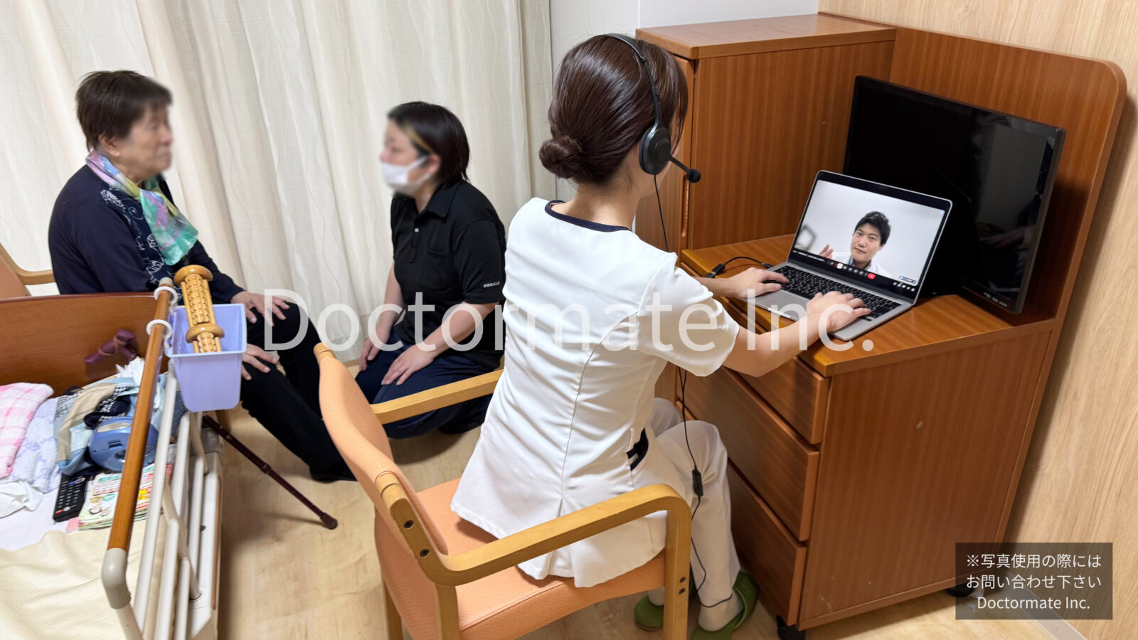 介護施設の個室で、利用者と介護職員がお話している様子と、手前にかけつけた看護師がノートパソコンを開いてインカムをつけ、画面ごしに医師と会話している様子を写した写真。かけつけの様子をあらわしています